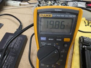 Testing Asus G513R charger voltage with a multimeter showing 19.86 volts